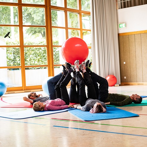 Patientinnen und Patienten halten mit den Beinen einen Ball in der Luft