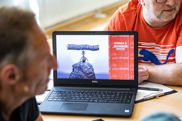 Zwei Personen sitzen an einem Laptop, auf dem man neben dem Schriftzug "Stärken & Ressoucen nutzen" das Bild einer Ameise sieht