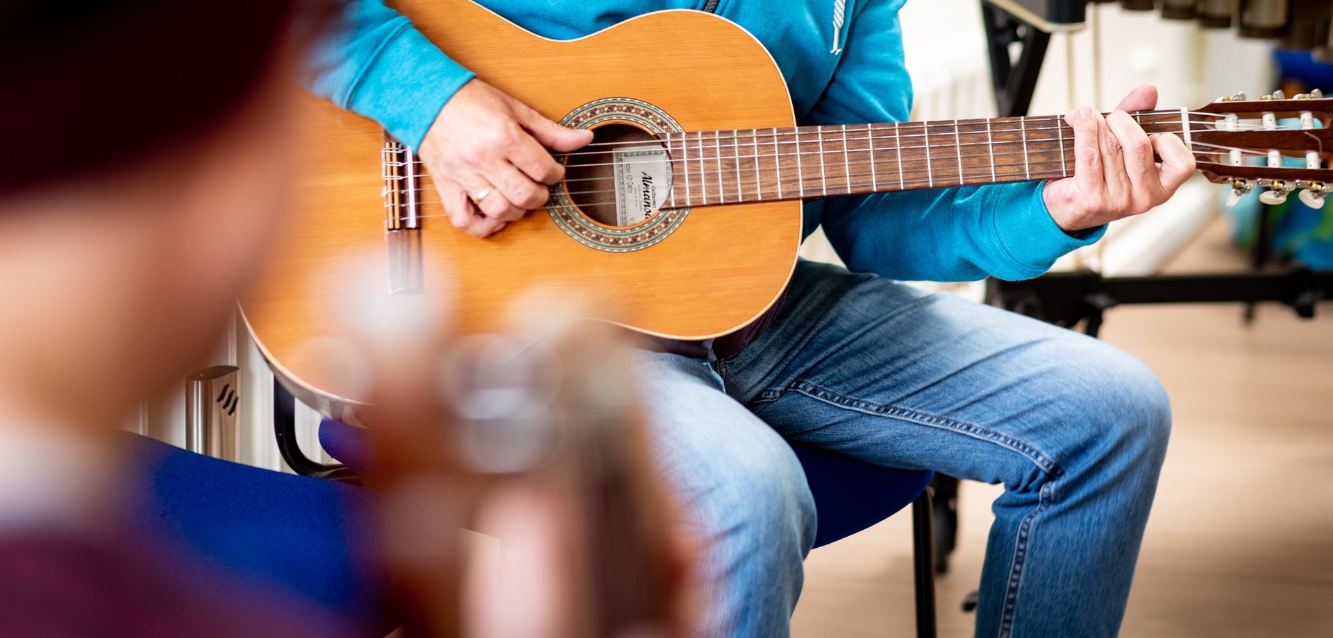 Ein Mann in einem türkisfarbenen Pulli und Jeans spielt auf einer Gitarre