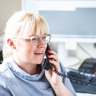 Portrait einer Mitarbeiterin, die in einem Büro am Schreibtisch sitzt und telefoniert